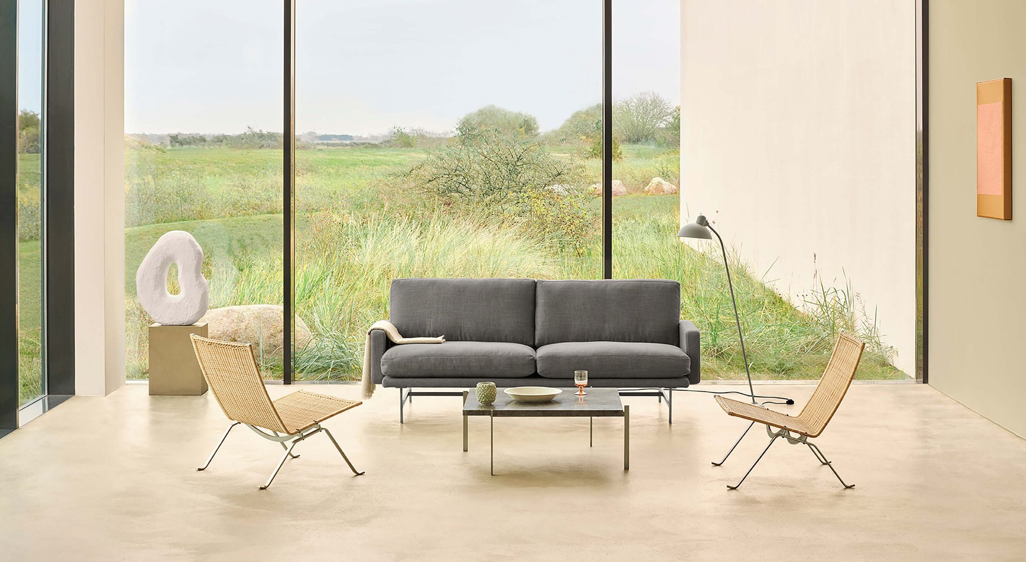 Mesa PK61 entre cadeiras PK22 e um sofá, numa sala com vista para o campo
